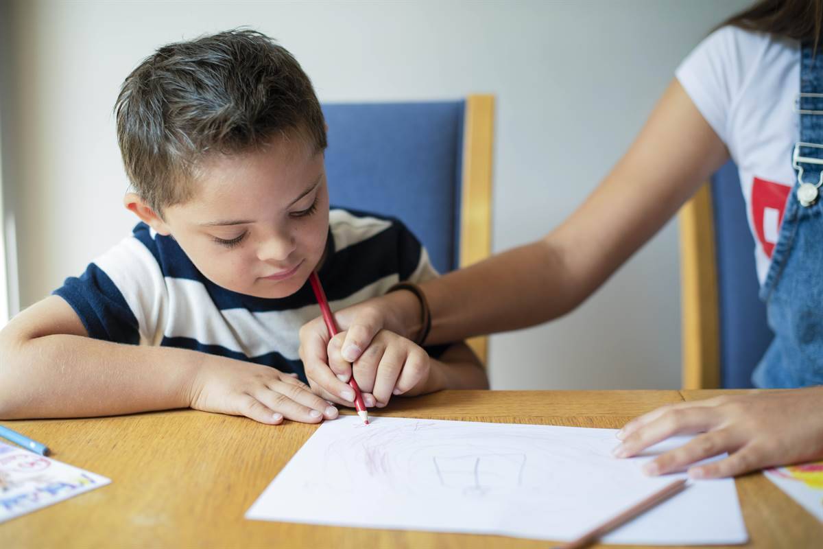 A girl helping her brother to make marks with a pencil