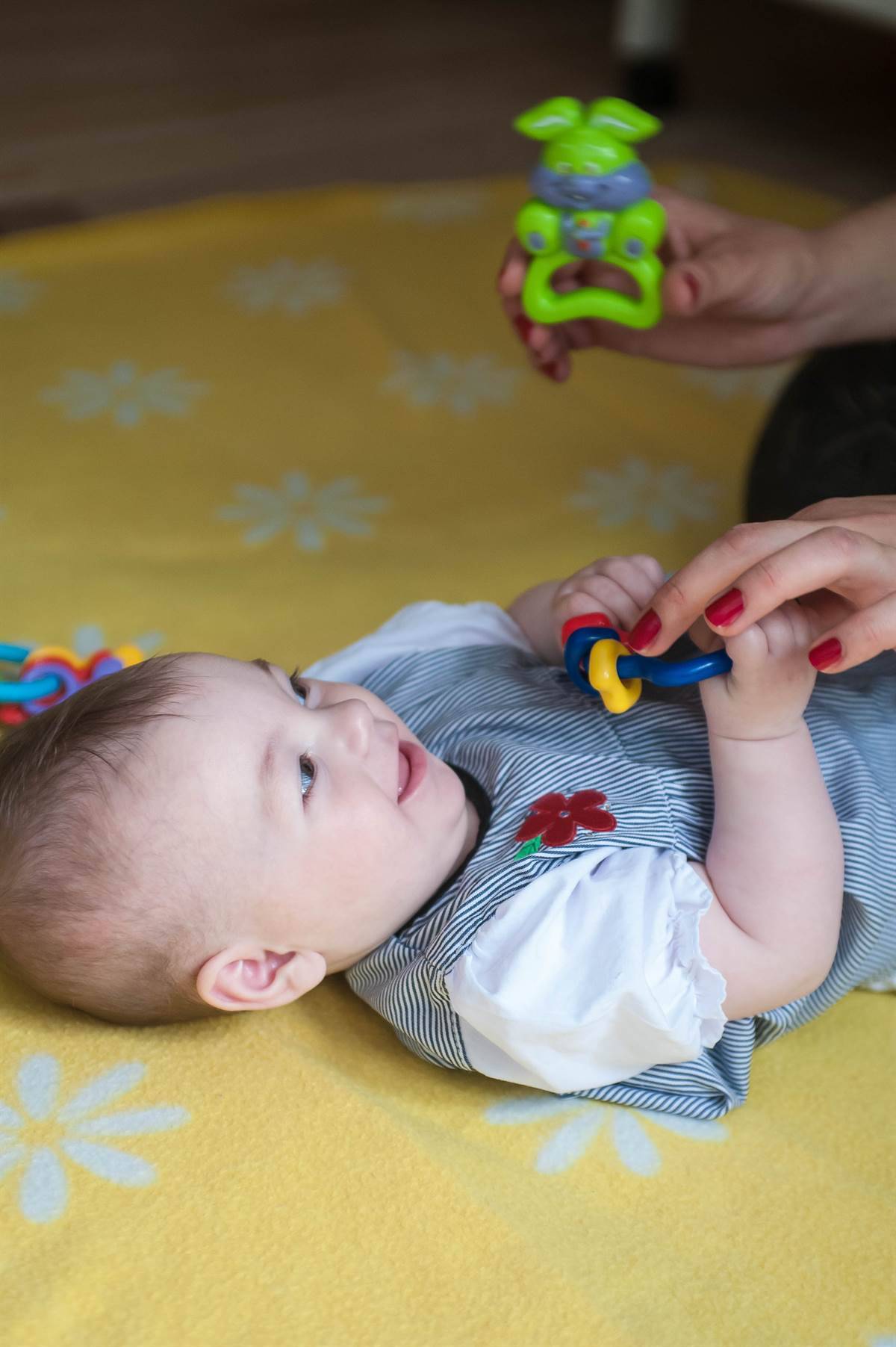beba u komunikaciji i interakciji sa odraslim koji drži igračke iznad bebe i provocira njenu reakciju