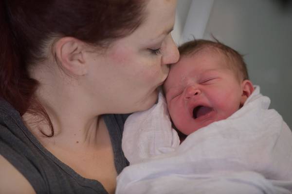 Mother kissing her newborn baby in the forehead.