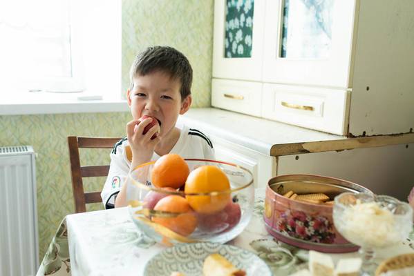 Boy (7 y.o), eats an apple as dessert after breakfast at home (Kazakhstan).