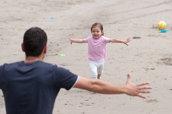 3 year old girl i is running into the arms of the father at the beach.