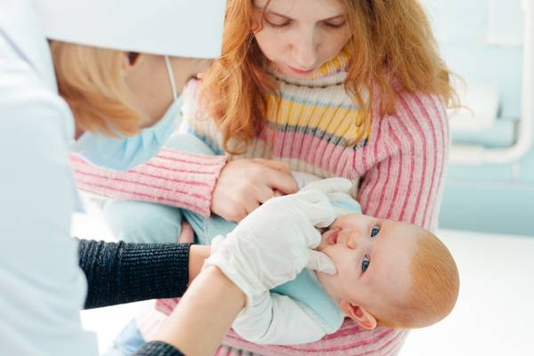 Nurse administers oral polio vaccine at a medical centre for a baby held by his/her mother.