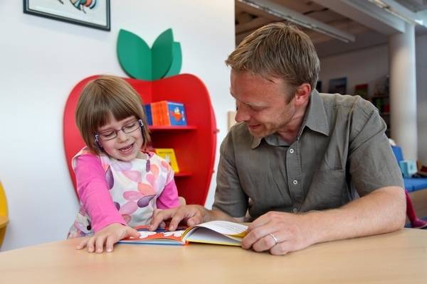 A young girl reads a picture book aloud with her father, at the public library.