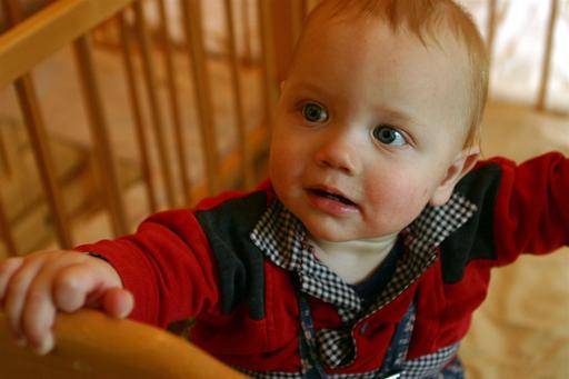 A baby standing holding the handrail of her or his bed