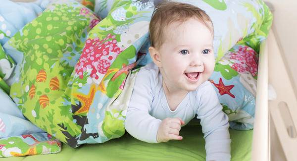 Smiling baby peeks out from under the blanket