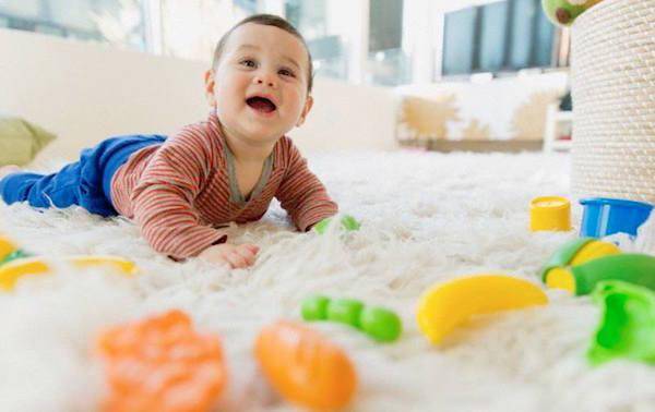 Smiling baby is crawling over the soft carpet with the toys around him or her