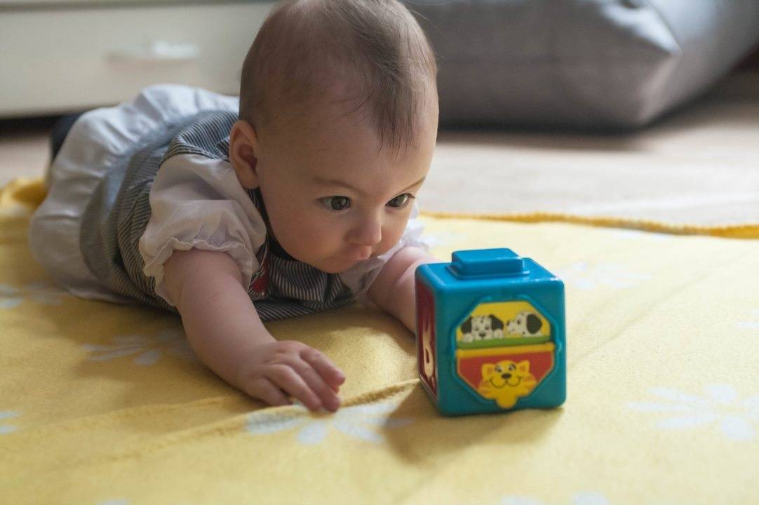 Малыш лежа на животе наблюдает и хватает игрушку
