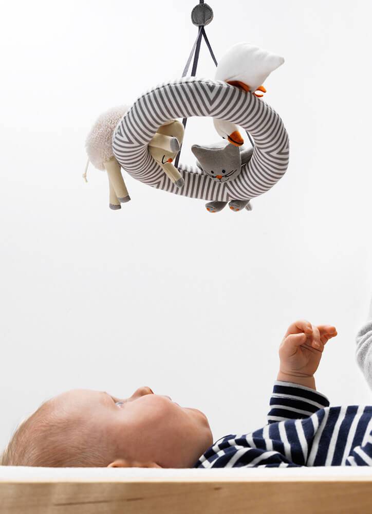 Baby is laying on his or her back and gazing on the toys hanging in front of him or her on the ceiling.