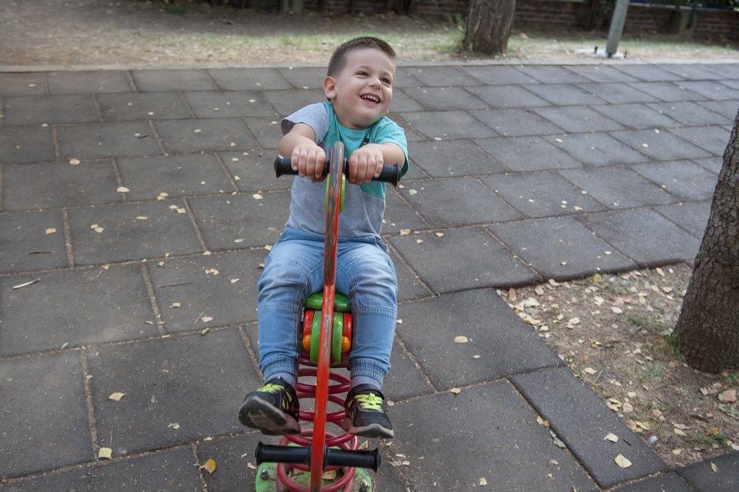 dečak se smeje dok se ljulja na spravi konjiću u dvorištu sa bezbednom podlogom