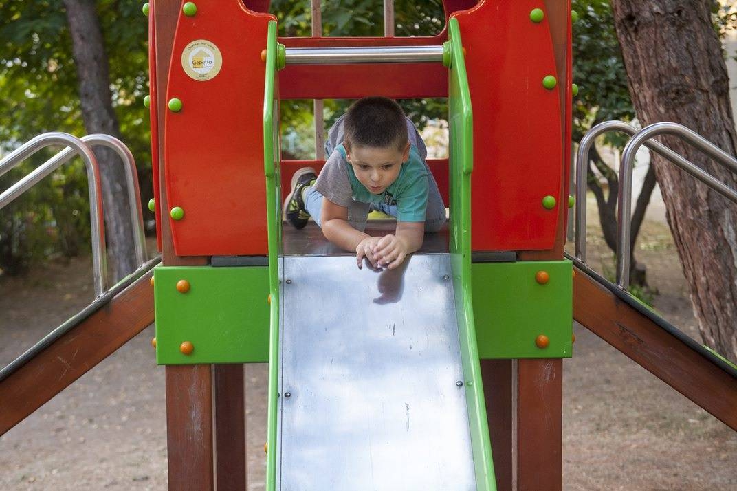A boy prepares to descend the slide with his arms and head forward