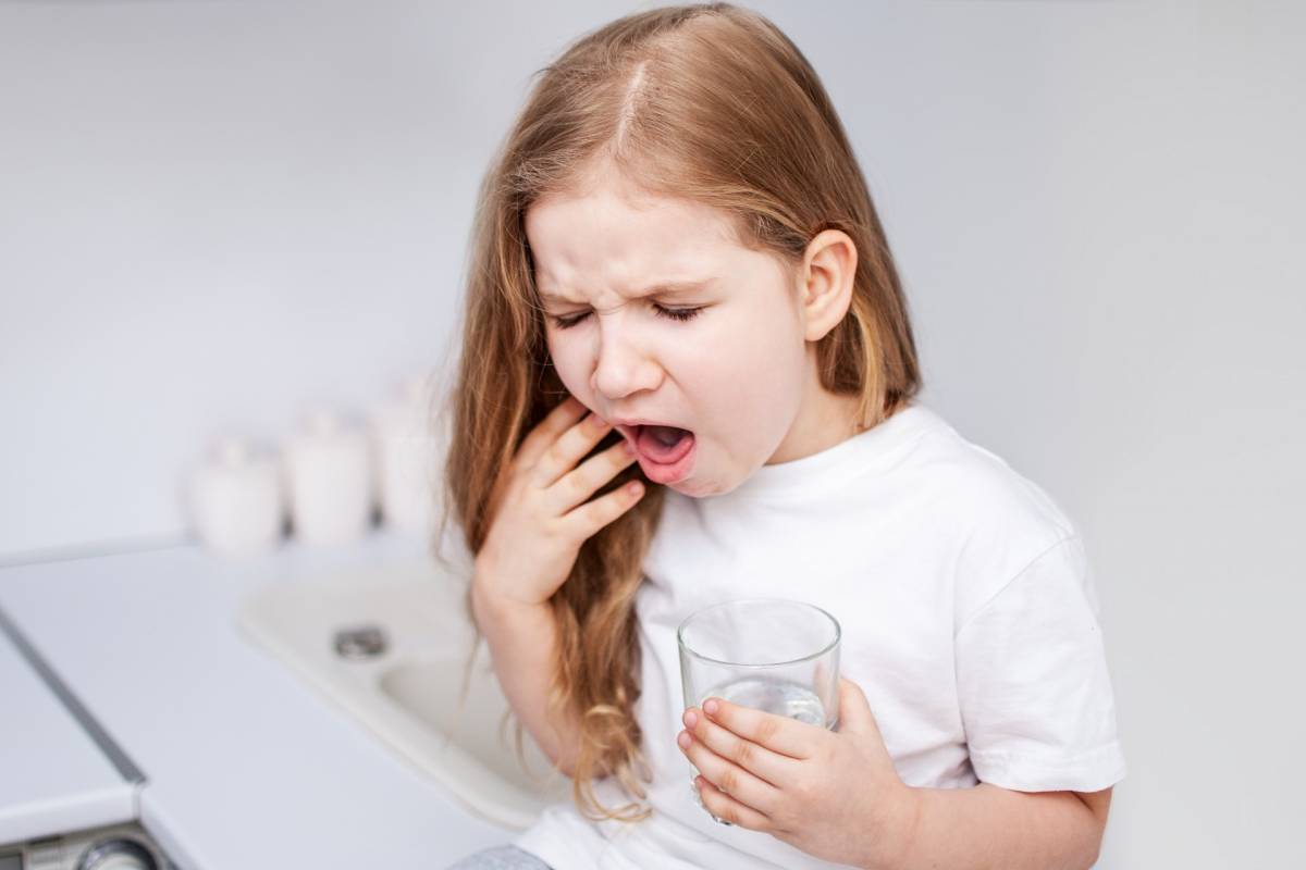 aA girl with a glass of water tries to cough up something that is suffocating her
