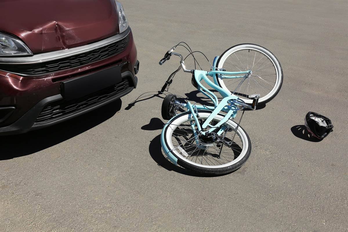 A bicycle and a helmet next to a damaged car