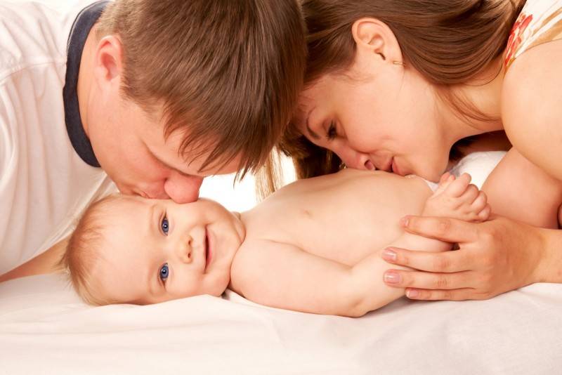 A mother and a father are kissing their smiling child 