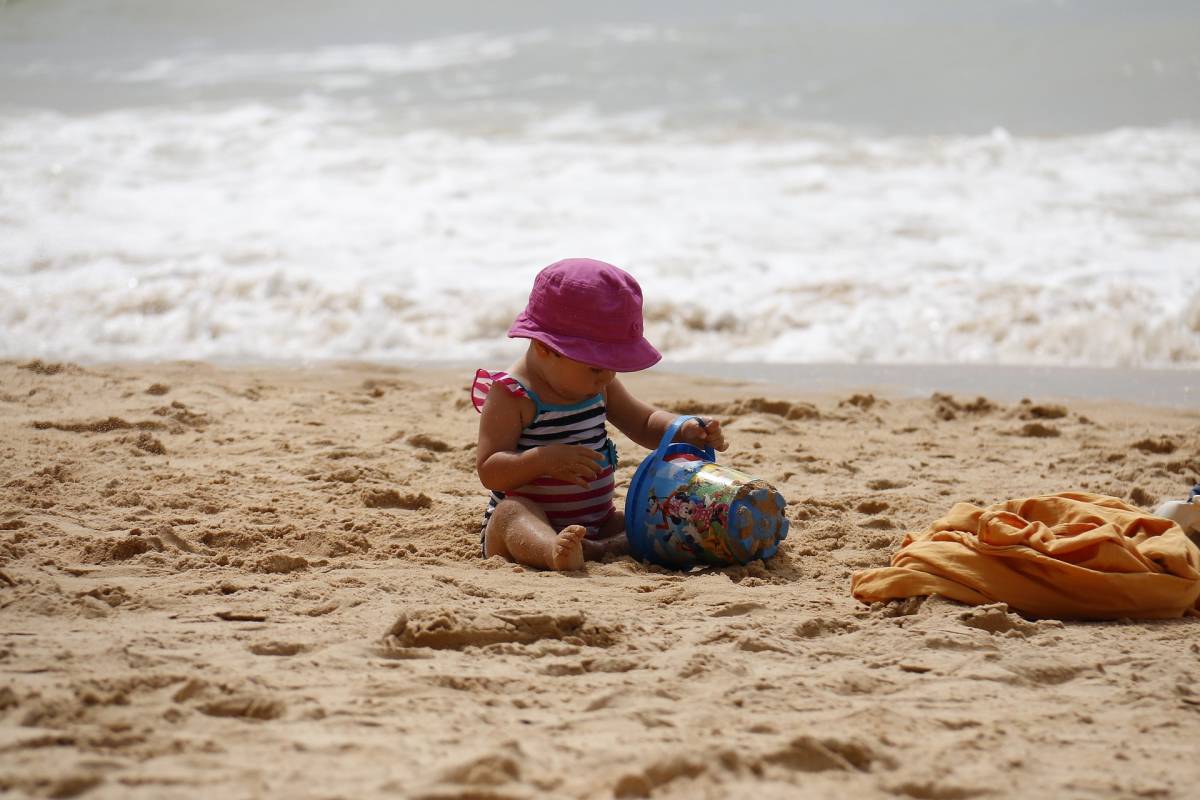 A child wearing a hat playing with the send in the beach 