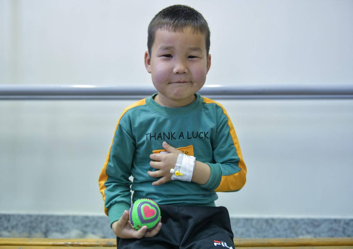4 year old boy sitting on a hospital bead, holding a ball