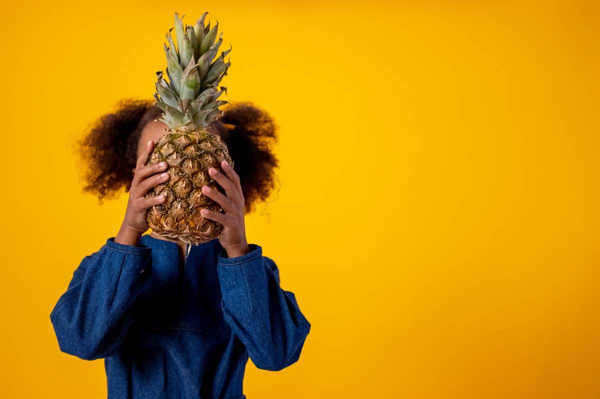 girl hiding her face behind a pineapple 