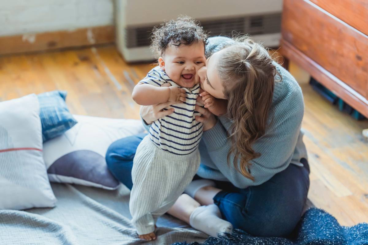 mother kissing baby, both sitting on the carpet