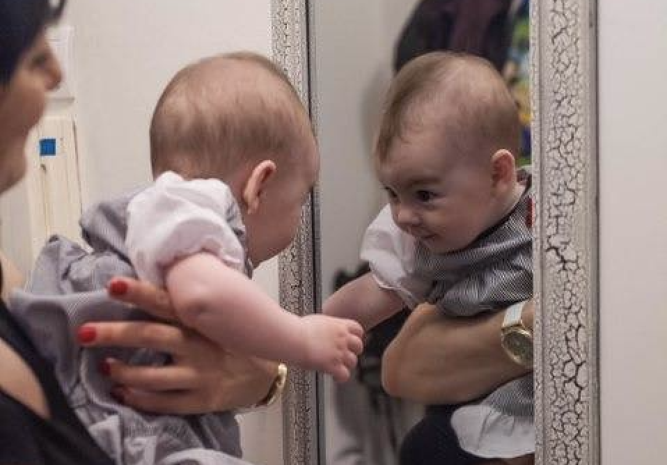 Caregiver holds infant in front of mirror