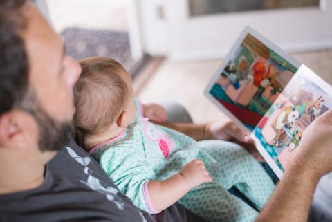 Father is reading a book to his child and talking 