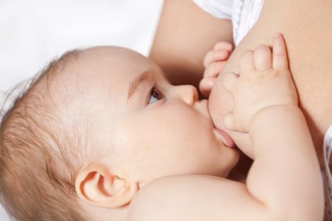 na slici je beba koja sisa, se rukicom drži za nabreklu dojku i gleda u majku