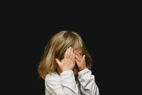 Toddler showing fear covering face with her arms