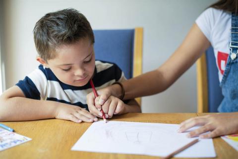 A girl helping her brother to make marks with a pencil