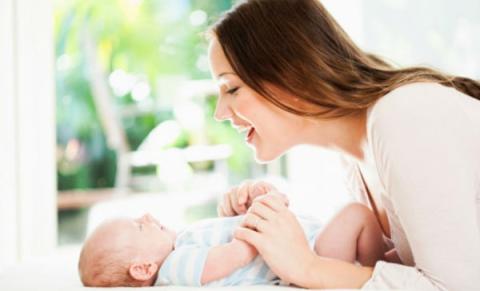 A mother smiling at the baby and holding her or his tiny hands
