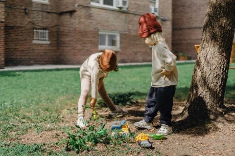 Two children playing together outside and trying to dig a hole in the ground
