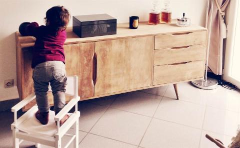 A baby is standing while playing with the objects situated over the commode