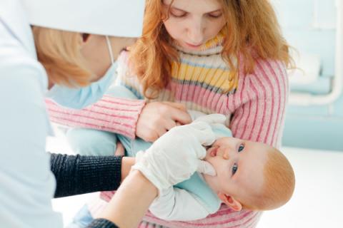 Nurse administers oral polio vaccine at a medical centre for a baby held by his/her mother.