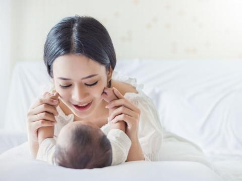 A baby lying on his or her back and touching her or his mother face with her or his tiny arms