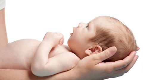 The parent is holding the baby supporting his or her head and the baby is attentively looking at the parent.