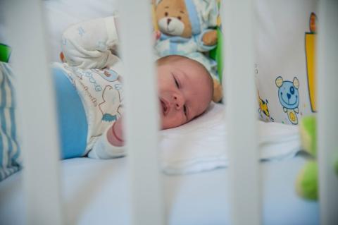 A baby lies on its side in the crib and plays on its own