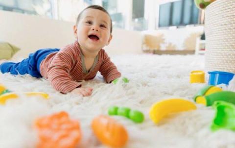 Smiling baby is crawling over the soft carpet with the toys around him or her