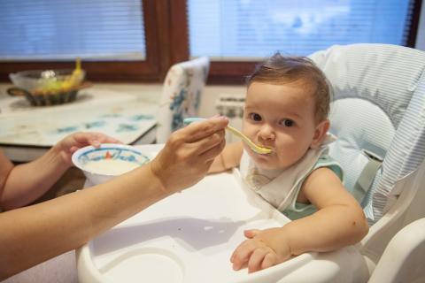 dok beba sedi u stoličici odrasli je hrani (kašom)