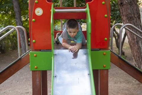 A boy prepares to descend the slide with his arms and head forward