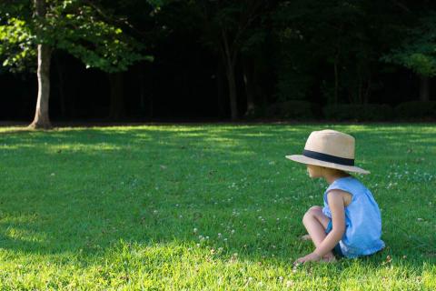 A girl seating in the grass with a hat on her head