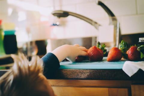 Toddler trying to reach some strawberries.