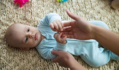 A baby laying on his or her back and touching his or her parent’s hand