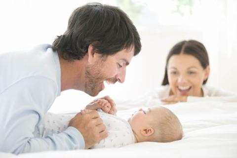 Father and mother are smiling and making sound while looking to their child lying on his or her back.