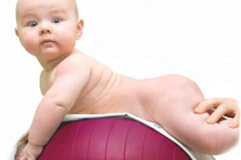 A child is lying on the ball on his or her tummy