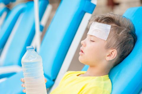 A child on a sunbed with a bottle of water and a cool cloth on his head