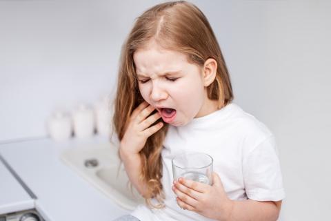aA girl with a glass of water tries to cough up something that is suffocating her