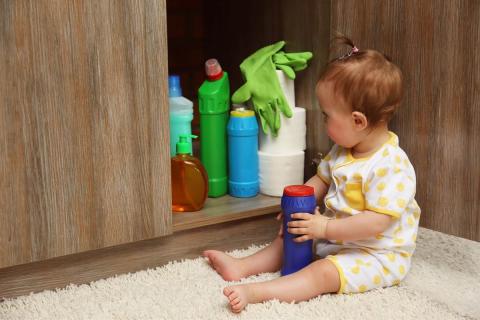 A baby in front of a closet with chemicals