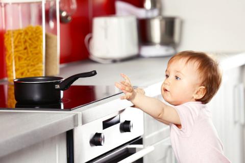 A baby trying to reach a pan placed over an unprotected stove