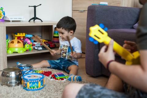 dečak svira na okrenutim šerpama kao da su bubnjevi, tata svira na dečijoj gitari-igrački
