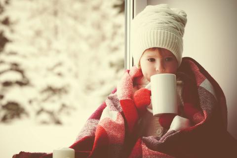 A child wearing a winter clothes with a cup of tea