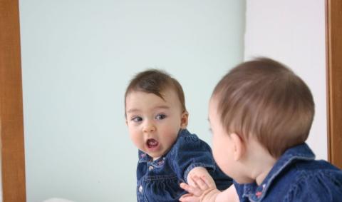A child is surprisingly looking at his or her reflection in the mirror