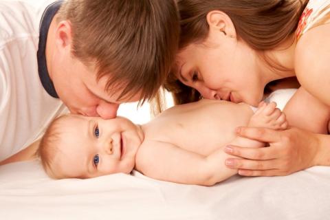A mother and a father are kissing their smiling child 