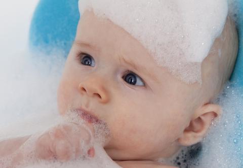 A baby taking bath with foam over his head 